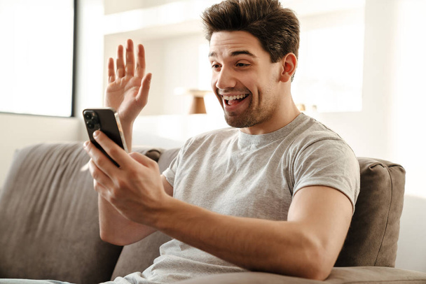 Happy man with smartphone having video call at home, waving hand - Foto, afbeelding