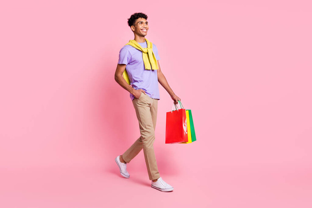 Full size photo of young handsome smiling afro man go shopping wear jumper on shoulders isolated on pink color background - 写真・画像