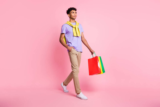 Full size photo of nice optimistic brunette guy go with bags wear t-shirt pants isolated on pink color background - Foto, Imagem