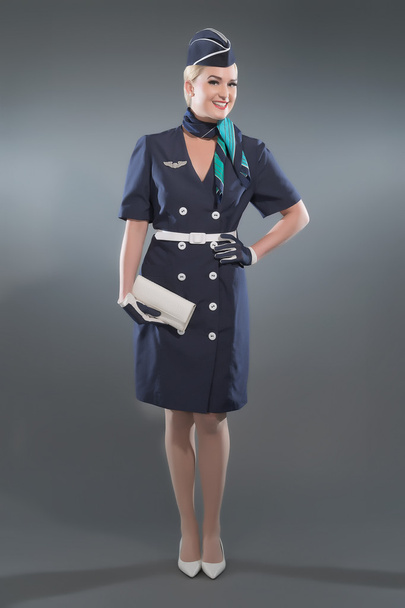 Smiling retro blonde stewardess wearing blue suit. Holding white - Fotoğraf, Görsel