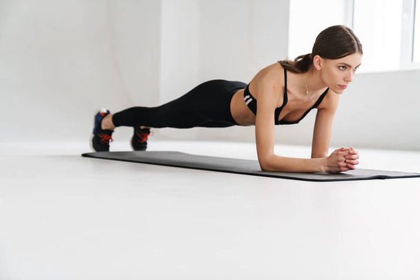 Athletic young sportswoman doing exercise while working out on mat indoors - Photo, Image