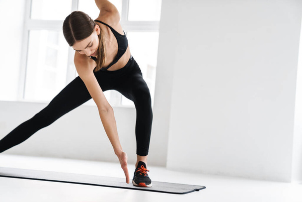 Athletic young sportswoman doing exercise while working out on mat indoors - Foto, Imagem