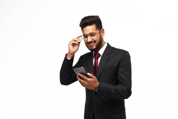 Portret van de jonge indiaanse manager met behulp van zijn telefoon op witte geïsoleerde achtergrond - Foto, afbeelding