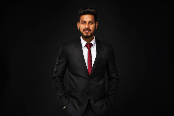 Portrait of young indian business man in black suit on black isolated background - Fotó, kép