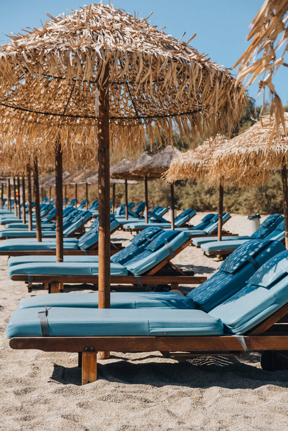 Fila de tumbonas azules vacías y tumbonas bajo las sombrillas en una playa en Mykonos, Grecia. - Foto, imagen