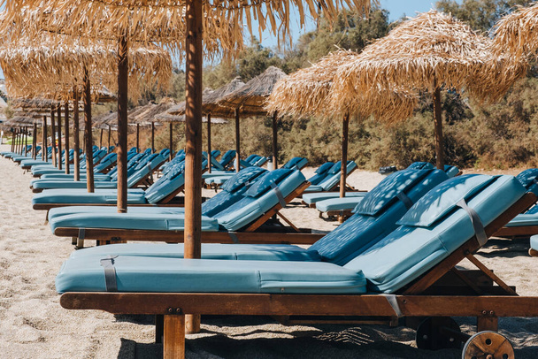 Fila de tumbonas azules vacías bajo las sombrillas en un soleado día de verano en una playa en Mykonos, Grecia. - Foto, imagen