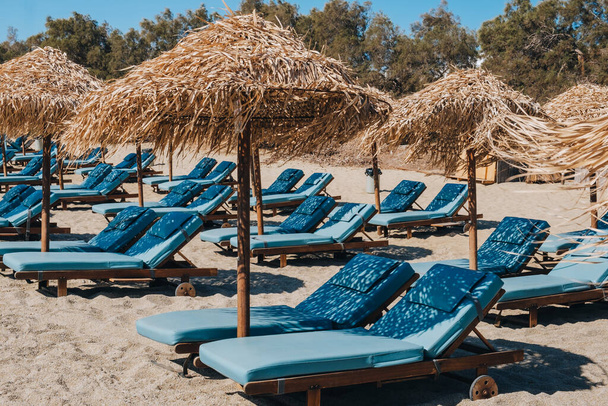 Tumbonas y tumbonas azules vacías bajo las sombrillas en una playa en Mykonos, Grecia. - Foto, imagen