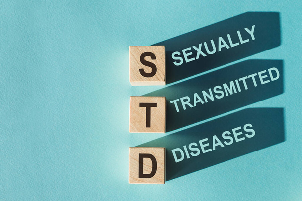 Wooden cubes building word STD - (abbreviation Sexually transmitted diseases) on light blue background. - Foto, Imagen