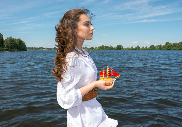 κορίτσι κατέχει ένα μικρό σκάφος με πανιά κόκκινο. σύγχρονες assol. - Φωτογραφία, εικόνα