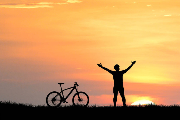 σιλουέτες του ανθρώπου και του ποδηλάτου με ουρανό ηλιοβασίλεμα στο παρασκήνιο - Φωτογραφία, εικόνα