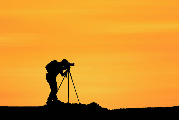 Silhouette eines Fotografen mit Kamera auf dem Hintergrund des Sonnenuntergangs - Foto, Bild