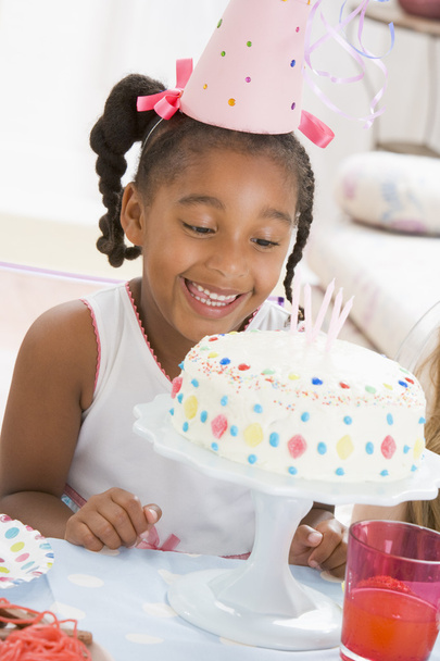 Young girl wearing party hat looking at cake smiling - Zdjęcie, obraz
