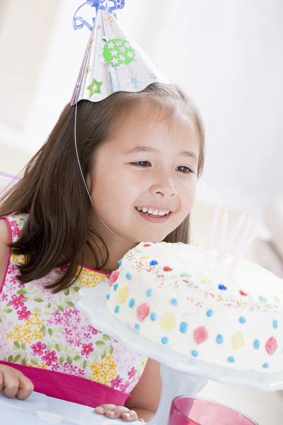 Young girl wearing party hat looking at birthday cake smiling - 写真・画像