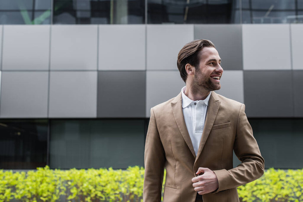 cheerful businessman unbuttoning blazer and looking away outside  - Fotoğraf, Görsel