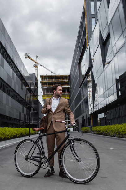 full length of businessman in suit holding bag and standing near bicycle outside  - Photo, image