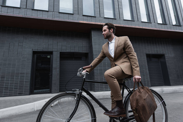 young businessman in formal wear holding leather brown bag and riding bicycle outside  - Zdjęcie, obraz