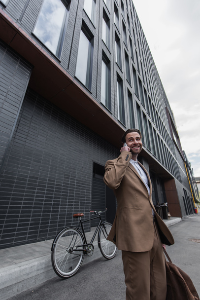 usmívající se obchodník ve formálním oblečení mluvit na smartphone venku - Fotografie, Obrázek