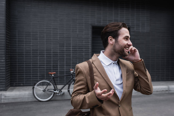happy young businessman in formal wear talking on smartphone outside - Фото, зображення