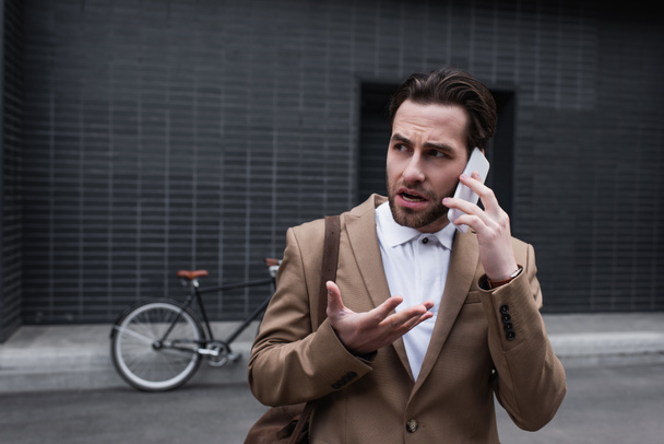 stressed young businessman in formal wear talking on smartphone outside - Foto, afbeelding
