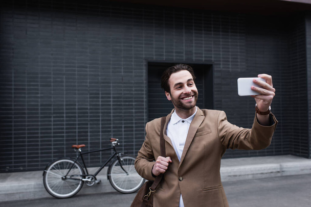 happy young businessman in formal wear taking selfie on cellphone outside - Fotó, kép