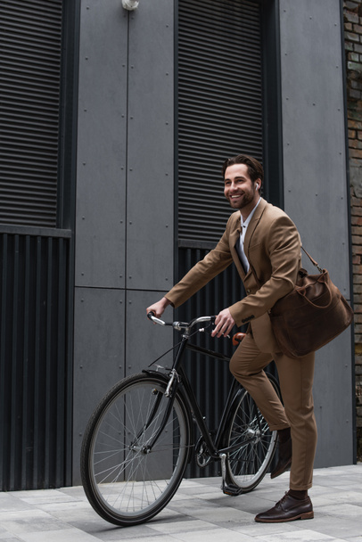 full length of happy businessman in earphones riding bicycle  - Photo, Image