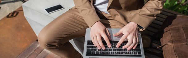 vista recortada de hombre de negocios escribiendo en el ordenador portátil mientras está sentado en el banco, pancarta - Foto, Imagen