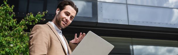 low angle view of businessman in earphones having video call on laptop outside, banner - Foto, Bild