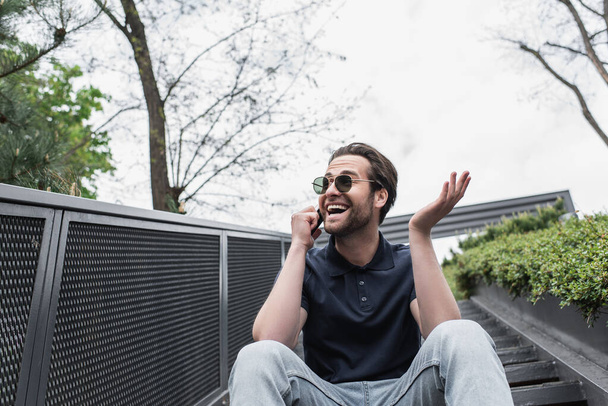 smiling man in sunglasses and polo shirt talking on cellphone outside  - Fotó, kép