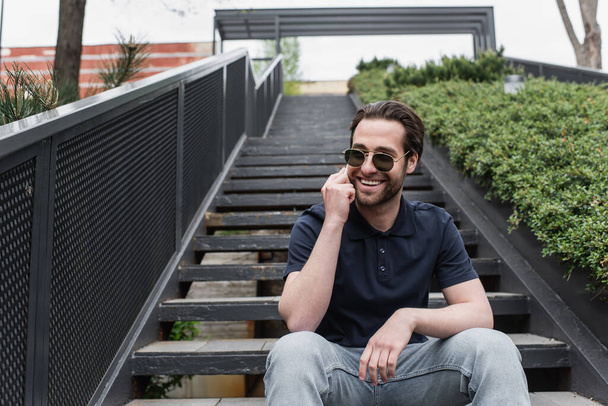 happy man in sunglasses and polo shirt talking on smartphone outside  - Foto, Bild