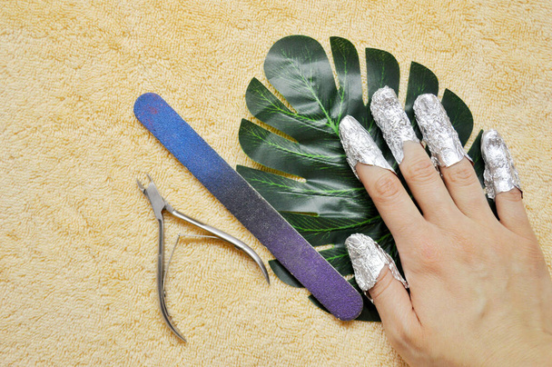 fingers with foil, wire cutters and nail file on leaf of palm on beige towel - Photo, Image