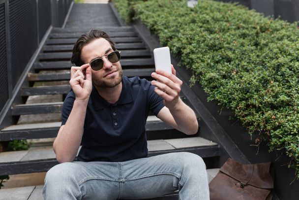 hombre feliz en gafas de sol y polo tomando selfie en el teléfono celular fuera - Foto, imagen