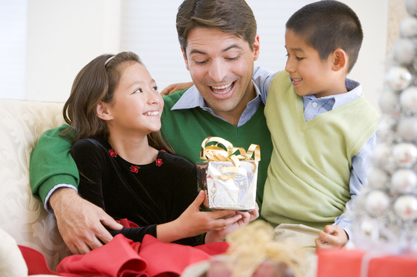 Father Being Given A Christmas Present By His Daughter And Son - 写真・画像