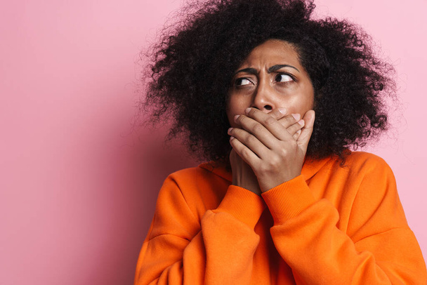 Displeased african american woman covering her mouth and looking aside isolated over pink background - Fotografie, Obrázek