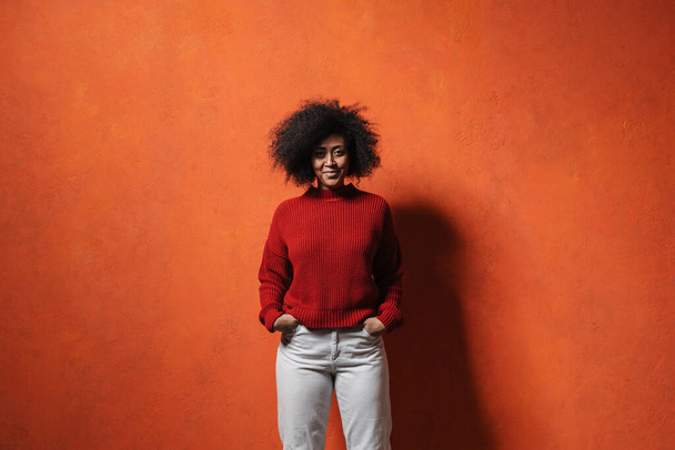 Cheerful young african woman wearing sweater posing standing isolated over red background. People lifestyle concept - Foto, Bild
