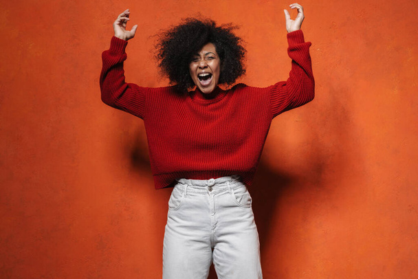 Cheerful young african woman wearing sweater posing jumping isolated over red background. People lifestyle concept - Foto, immagini