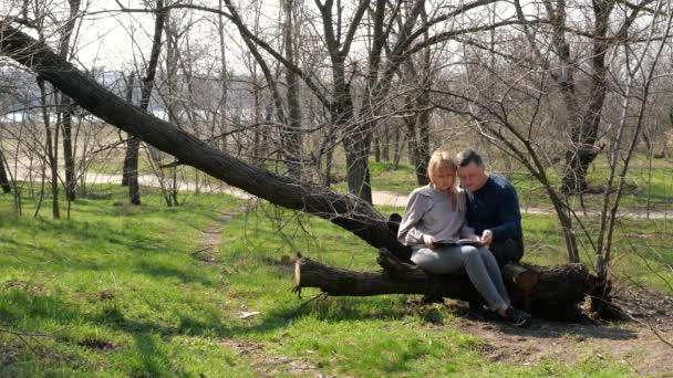 Man and woman are sitting on tree and reads book - Imágenes, Vídeo