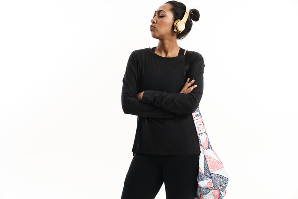 Confident african american woman in headphones posing with fitness bag isolated over white background - Fotoğraf, Görsel