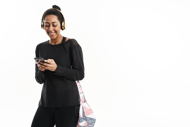 Mujer afroamericana sonriente en auriculares usando teléfono celular aislado sobre fondo blanco - Foto, Imagen
