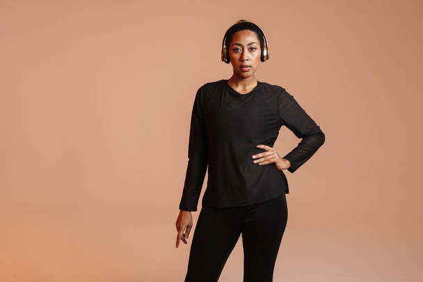 Confident african american sportswoman posing in wireless headphones isolated over beige background - Foto, immagini