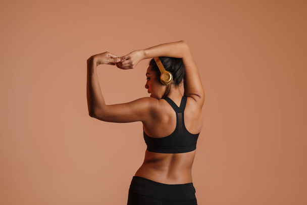 Focused african american woman in headphones doing exercise while working out isolated over beige background - Foto, imagen
