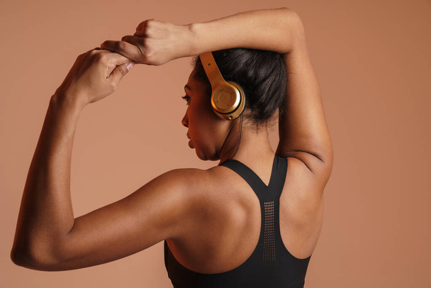Focused african american woman in headphones doing exercise while working out isolated over beige background - Fotografie, Obrázek