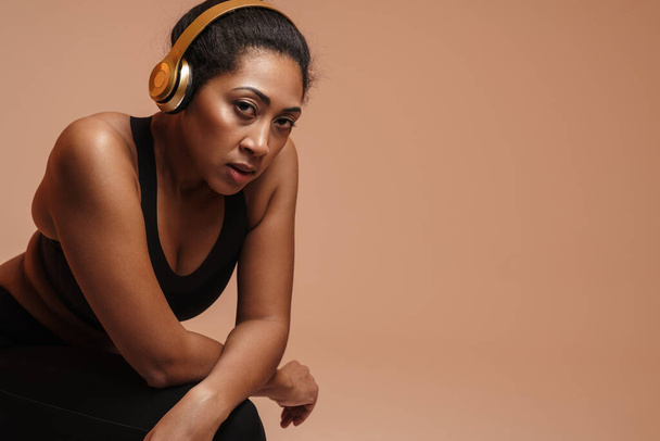 Focused african american woman in headphones doing exercise while working out isolated over beige background - Fotoğraf, Görsel