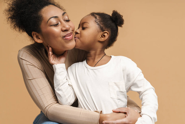 Happy black mother and daughter hugging and kissing isolated over beige background - Φωτογραφία, εικόνα