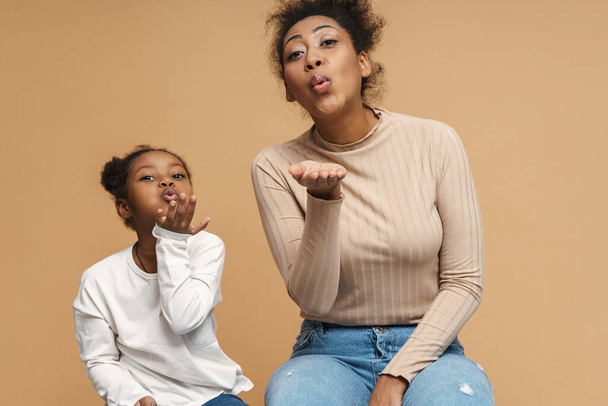Happy black mother and daughter blowing air kiss at camera isolated over beige background - Fotó, kép