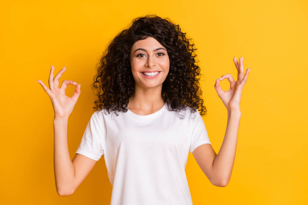 Photo of young smiling happy positive lovely pretty girl showing okay sign wear white t-shirt isolated on yellow color background - Φωτογραφία, εικόνα
