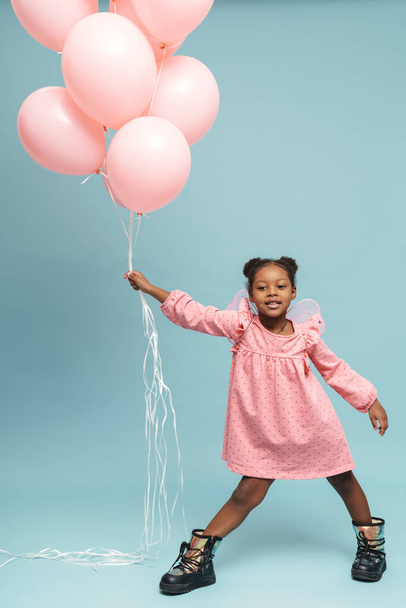 African girl wearing pink dress posing with balloons isolated over blue wall - Fotografie, Obrázek