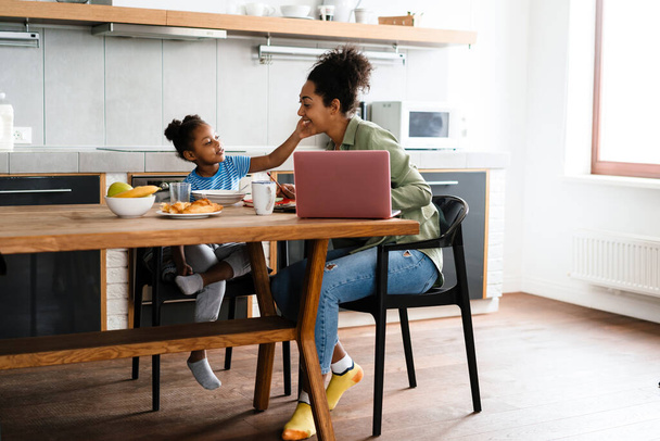 Happy mother and daughter having breakfast at table in home kitchen - Foto, Bild