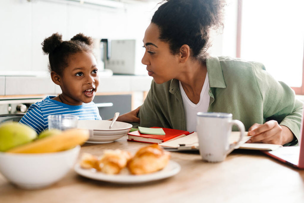 Black mother and daughter having breakfast at table in home kitchen - Foto, Imagen