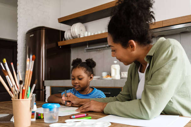 Black mother drawing with her daughter at table in home kitchen - Foto, Imagem