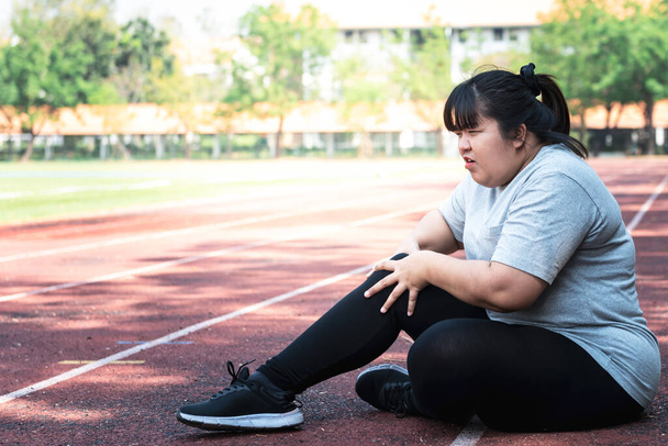 Azjatycka gruba kobieta, ma obecnie kontuzję kolana Podczas ćwiczeń biegając po torze biegowym w parku, z powodu choroby zwyrodnieniowej stawów, do sportu i opieki zdrowotnej koncepcji. - Zdjęcie, obraz